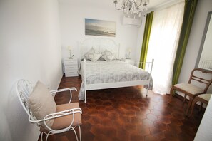 Un dormitorio con una cama, dos mesitas de noche, una silla, una araña y un cuadro en la pared.