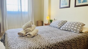 A neatly made bed with rolled towels, a patterned bedspread, and two framed artworks on the wall. - Albatros 1 by At Home Costa del Sol (Algarrobo)