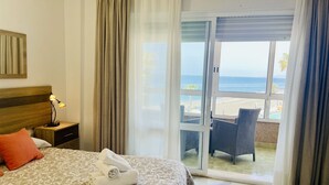 Et hotelværelse med en seng, et natbord med lampe, et vindue med gardiner og udsigt til stranden.