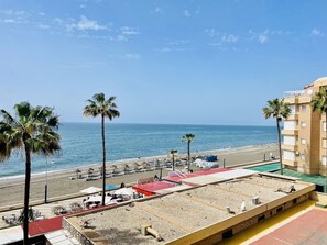 Vista da praia com palmeiras, um edifício com restaurante e céu claro.