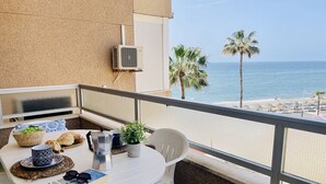 En balkon med et bord til to, en potteplante og udsigt til stranden og palmer.