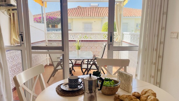 Ein Essbereich mit Tisch für zwei Personen, einer Kaffeekanne, Obstschale und einem Teller Croissants.