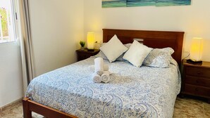 Ein ordentlich bezogenes Bett mit einem gemusterten Überwurf, zwei Nachttischlampen und einem Kunstwerk an der Wand darüber.