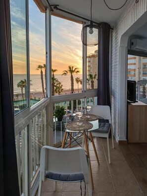 Een balkon met een glazen tafel, twee stoelen en een hanglamp.
