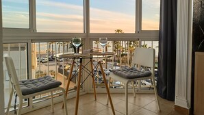 A balcony with a glass table, two cushioned chairs, and a view of the street and palm trees. - Ruselo 308 by At Home Costa del Sol (Torrox)