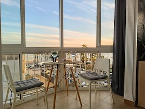 A balcony with a glass table, two cushioned chairs, and a view of the street and palm trees. - Ruselo 308 by At Home Costa del Sol (Torrox)