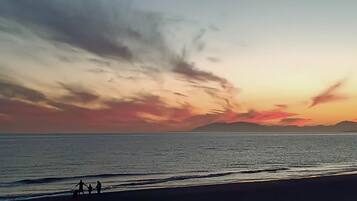 A beach scene with a sunset, calm sea, and silhouettes of two people walking.