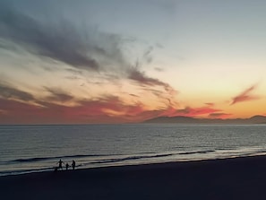 A beach scene with a sunset, calm sea, and silhouettes of two people walking. - Ruselo 308 by At Home Costa del Sol (Torrox)