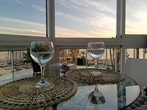 Een balkon met twee glazen tafels, elk met een gevlochten onderzetter en een glas water.