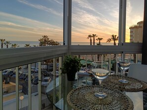 Een balkon met uitzicht op het strand, een tafel met een glas, en een parkeerplaats.