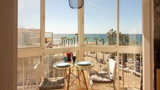 A balcony with a view of the beach, a glass table, two chairs, and a hanging light fixture. - Ruselo 308 by At Home Costa del Sol (Torrox)