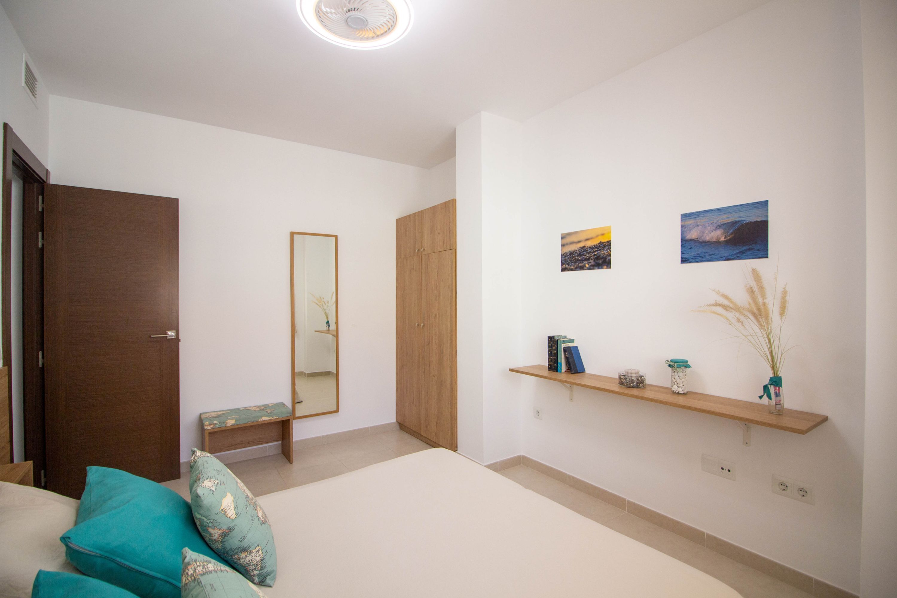 Una camera da letto con un letto, un armadio in legno, una panca, una mensola con oggetti decorativi e due quadri appesi al muro.