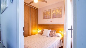 Une chambre à coucher avec un lit, une tête de lit en bois, deux lampes fixées au mur et un ventilateur de plafond.