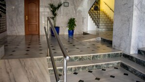 Un hall au sol en marbre, doté d’une porte en bois, de plantes en pot et d’un escalier.