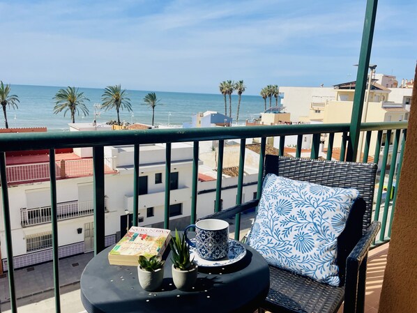 A balcony with a view of the sea, a wicker chair, a small table with a book, a mug, and two potted plants. - Albatros 3 by At Home Costa del Sol (Algarrobo)