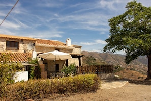 A stone building with a tiled roof, a wooden fence, and a view of hills. - Casa Esparragueras by At Home Costa del Sol (Còmpeta)
