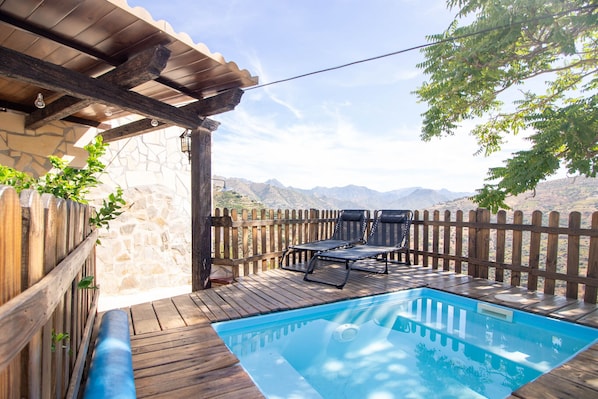 A wooden deck with a swimming pool, lounge chairs, and a stone wall. - Casa Esparragueras by At Home Costa del Sol (Còmpeta)