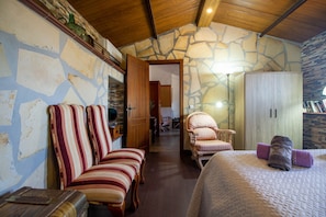 A room with a stone wall, wooden ceiling, a bed with a quilt, striped chairs, a wooden wardrobe, and a lamp. - Casa Esparragueras by At Home Costa del Sol (Còmpeta)