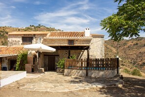 A stone house with a tiled roof, a fenced patio, and a hillside backdrop. - Casa Esparragueras by At Home Costa del Sol (Còmpeta)