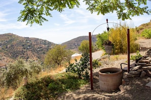 A rural landscape with a stone wall, a large clay pot, and hanging planters. - Casa Esparragueras by At Home Costa del Sol (Còmpeta)