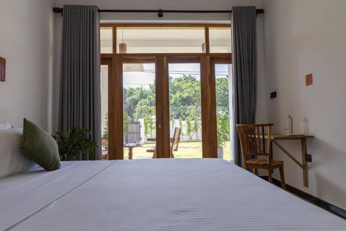 Una camera da letto con un letto grande, una sedia di legno, un tavolino e vista all'esterno tramite una porta scorrevole.