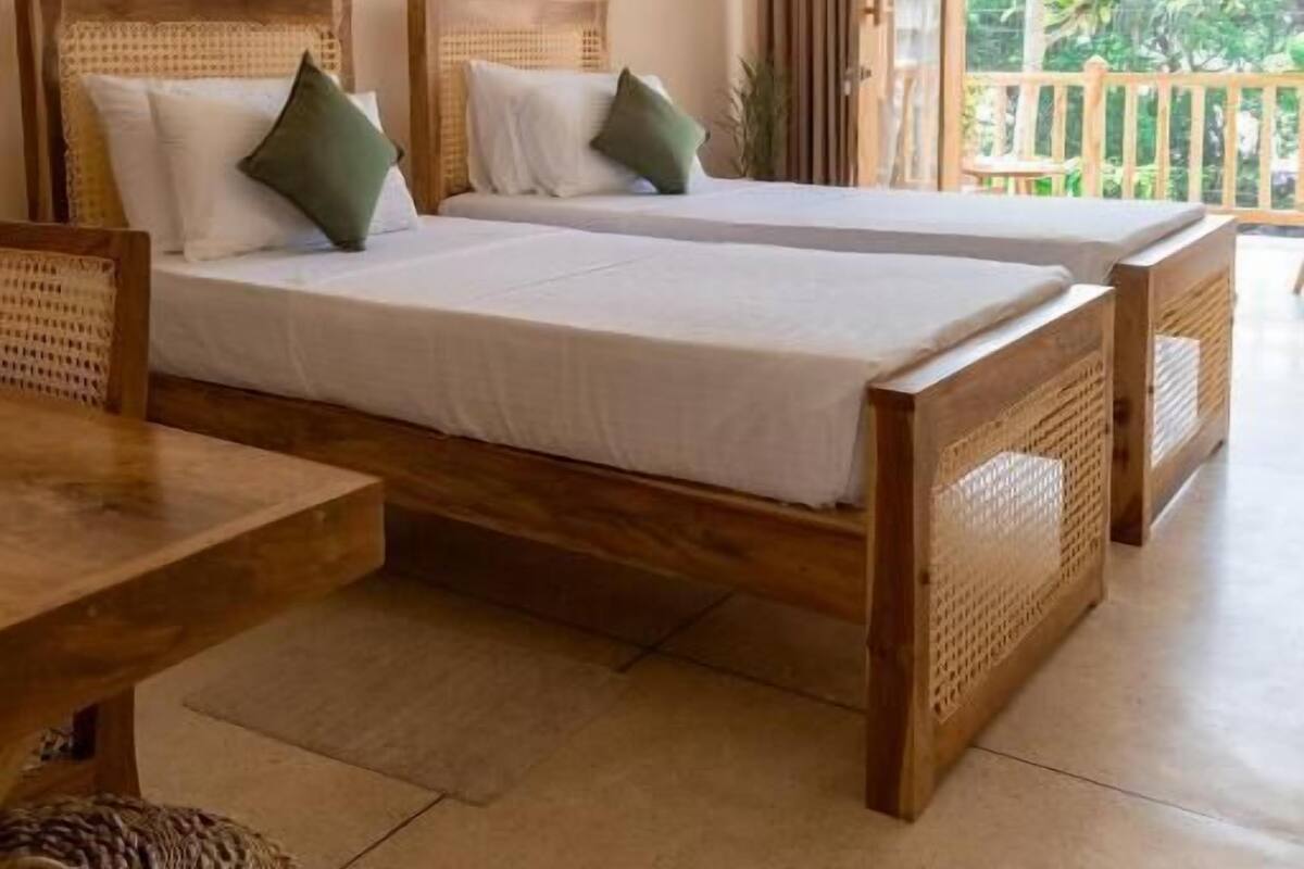 Una stanza con due letti di legno, una ventola a soffitto e un balcone con vista sul verde.