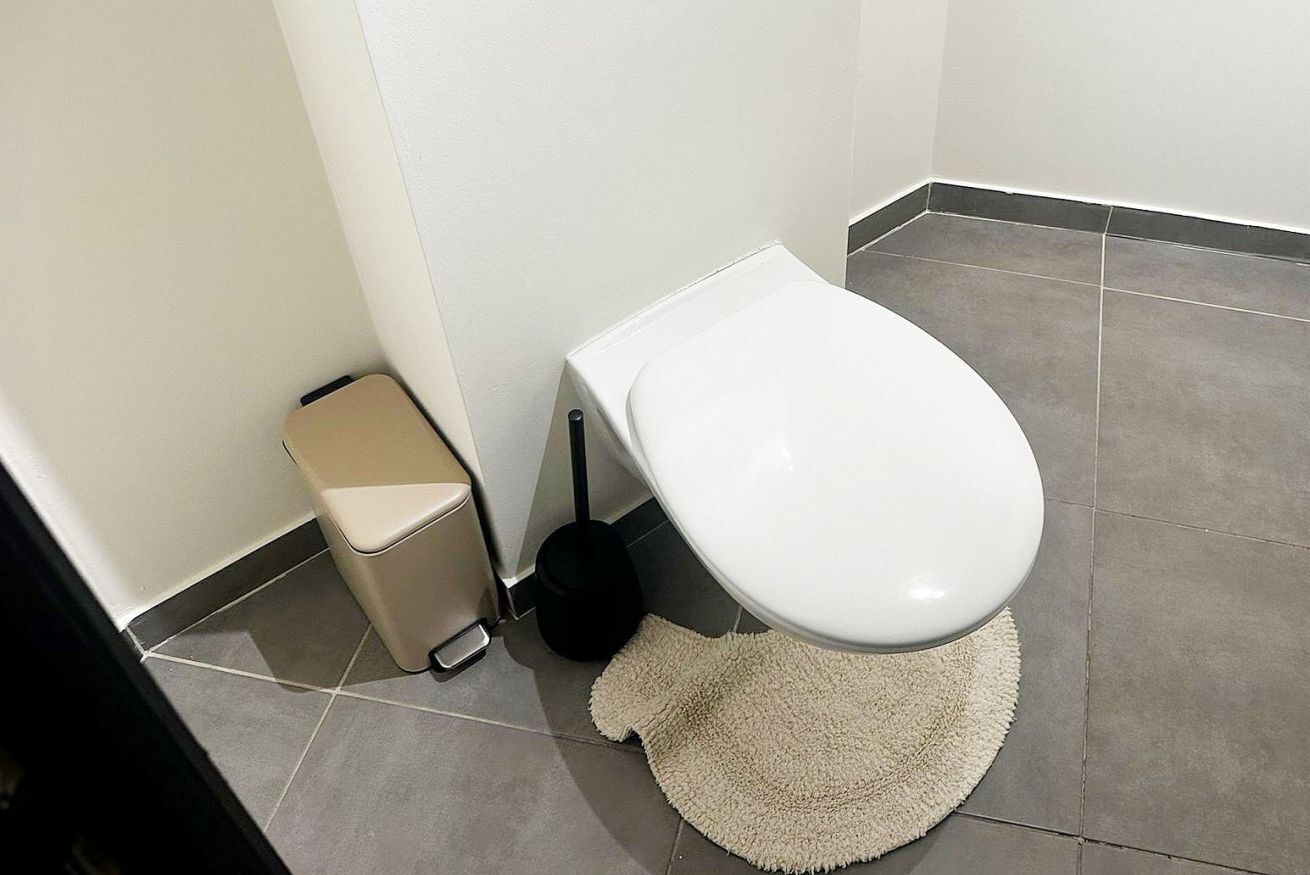 Un baño con inodoro, un cesto de basura y una alfombra en el suelo.