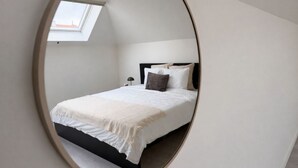 Et soveværelse med ovenlys, en seng med hvide sengetæpper, en sort sengegavl og et natbord.