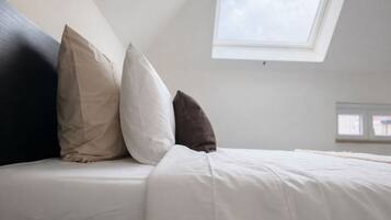 A bed with white bedding and three pillows in a room with a skylight.