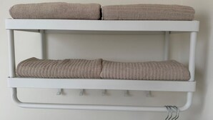 Et hvidt metalreol med to hylder, hver med et sammenrullet, beige håndklæde.