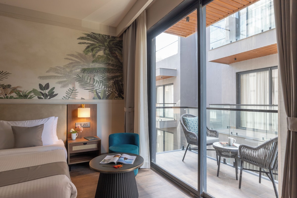 Et hotelværelse med balkon, seng, natbord, et bord med et magasin og en stol.
