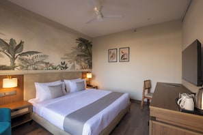 Habitación de hotel con cama, lámparas de noche, escritorio con silla, televisor y un cuadro en la pared.