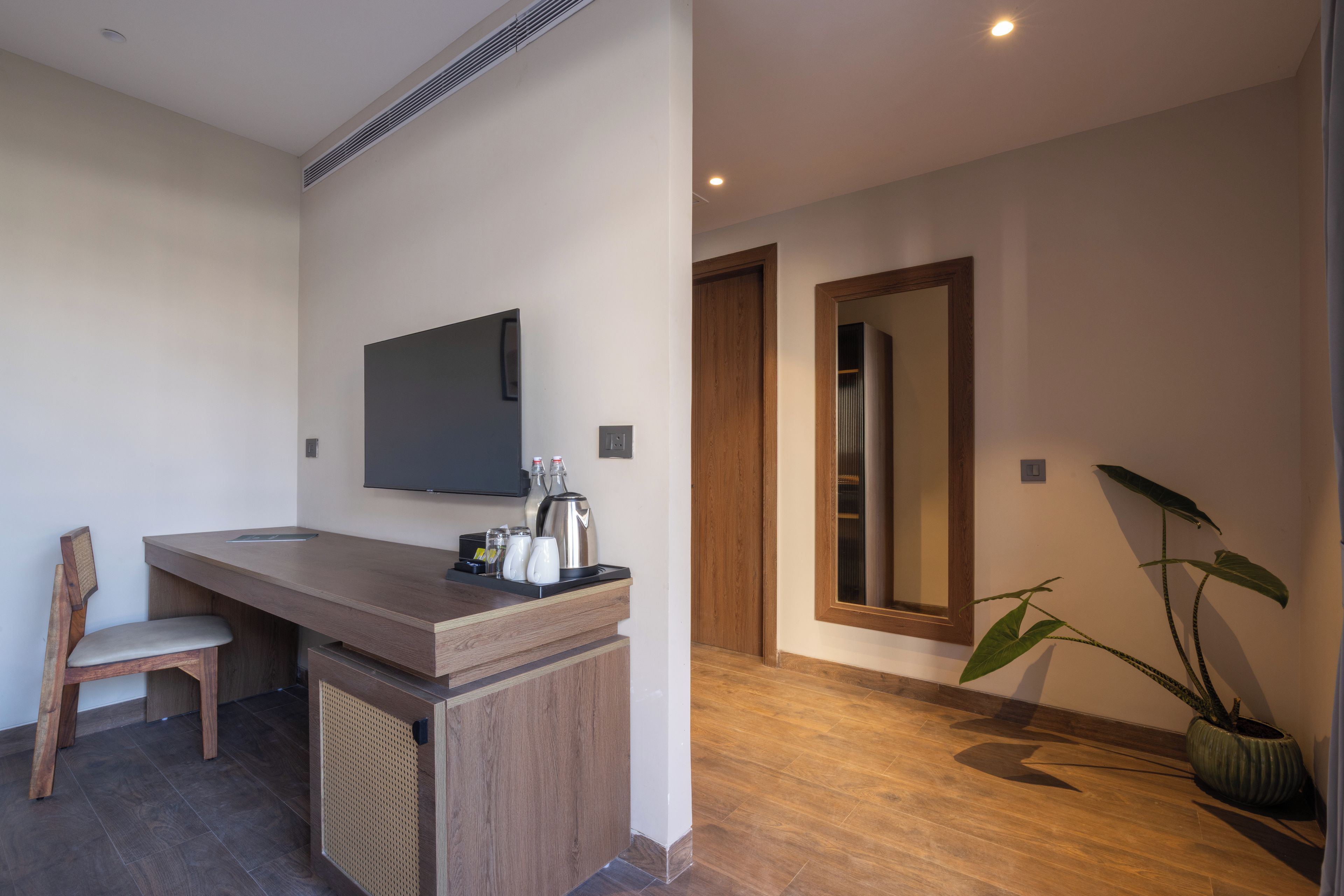 Un baño moderno con tocador de madera, un televisor de pantalla plana sobre el espejo y una planta en maceta.