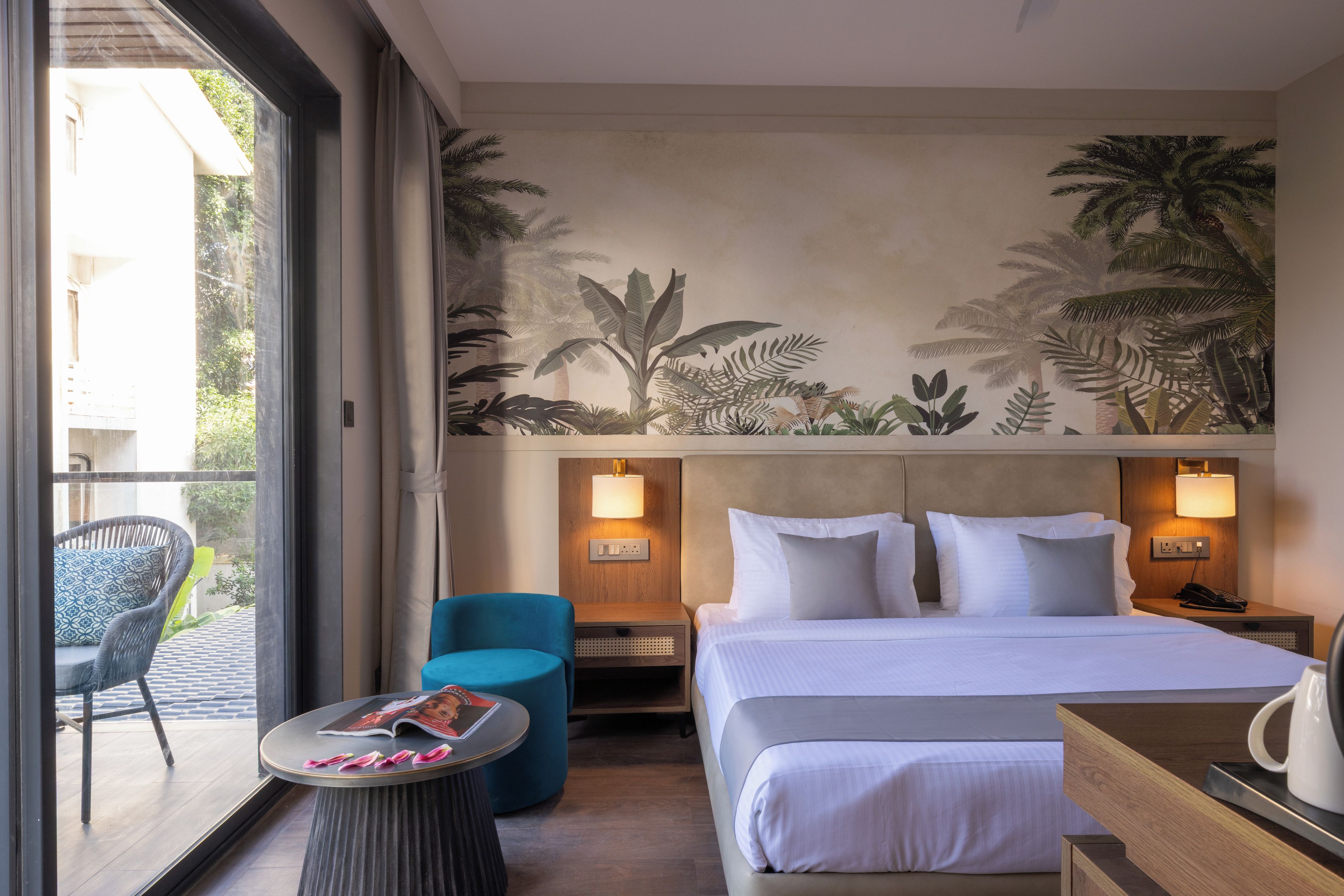 Una habitación de hotel con cama, mesita de noche, una silla, una pequeña mesa y un mural en la pared.