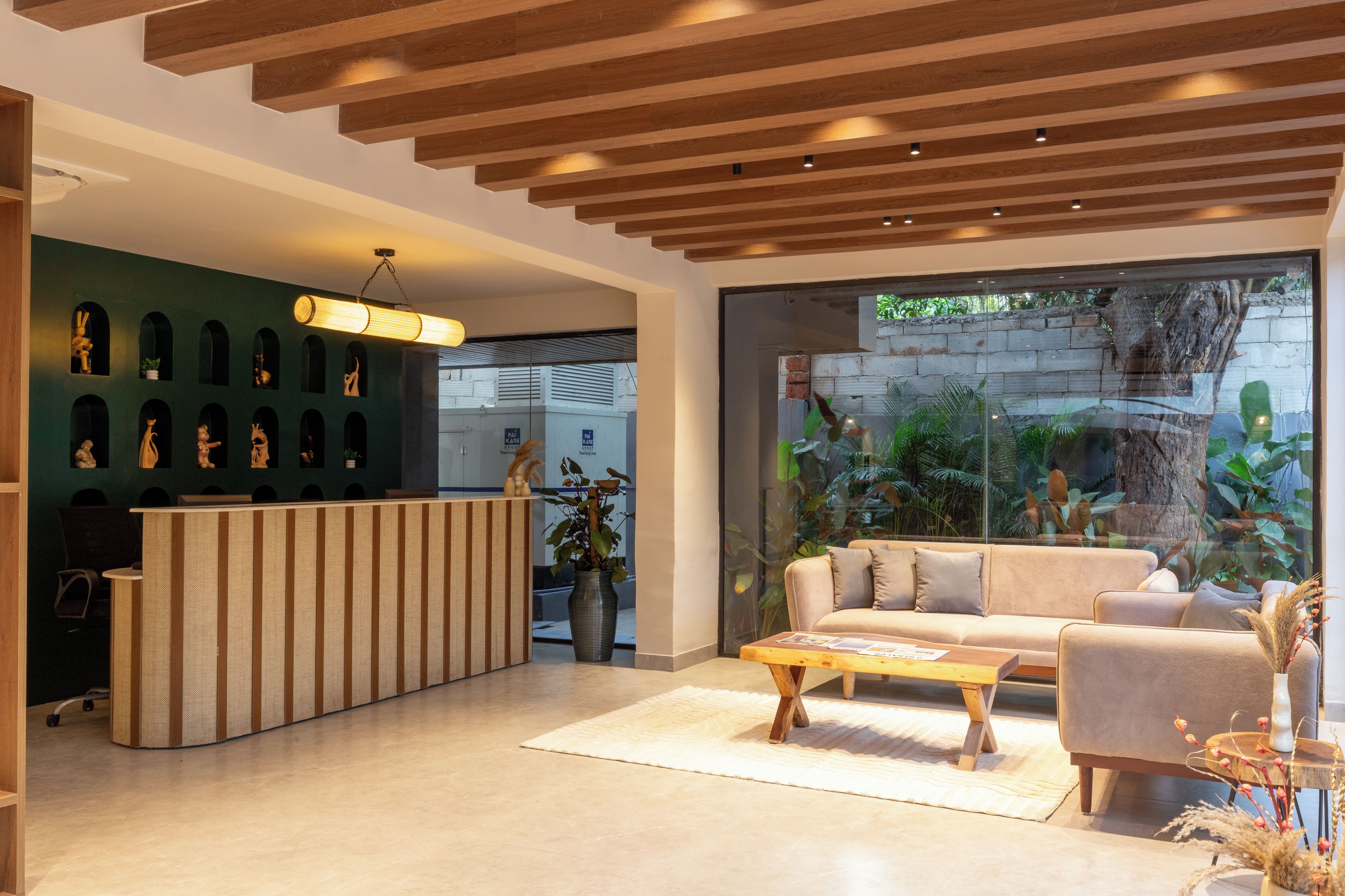 Un espace d’accueil moderne avec un comptoir de réception en bois, un mur végétal agrémenté d’œuvres d’art, une grande fenêtre donnant sur un paysage verdoyant et un canapé beige.