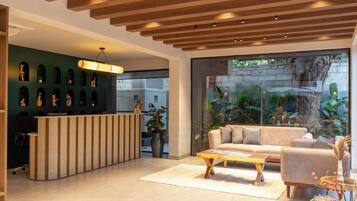 Un'area reception moderna con una scrivania in legno, una parete verde decorata con opere d'arte, un'ampia finestra vista su vegetazione e un divano beige.