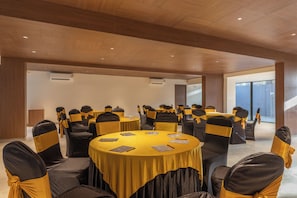 Un salón de conferencias con mesas redondas, sillas con cintas amarillas y techo de madera.