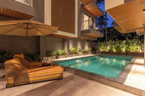 A modern outdoor pool area with a lounge chair and umbrella, surrounded by plants and a view of the sky. - Sibaya Courtyard By Stone Wood Premier (Baga)