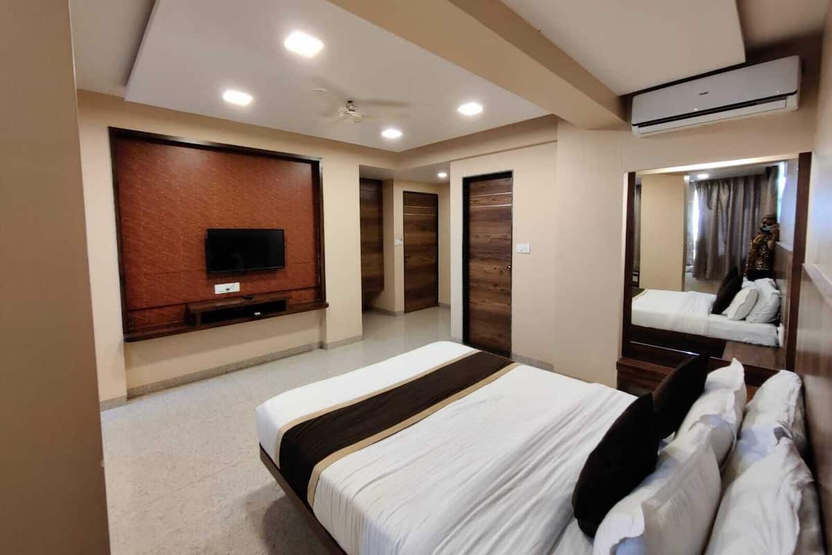 A hotel room with a bed, a television, a ceiling fan, and an air conditioning unit.