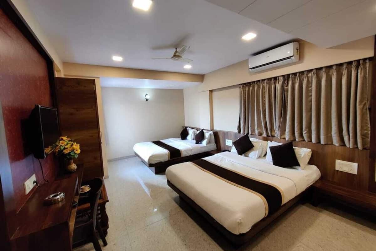 A hotel room with two beds, a desk with a chair, a television, and an air conditioning unit.
