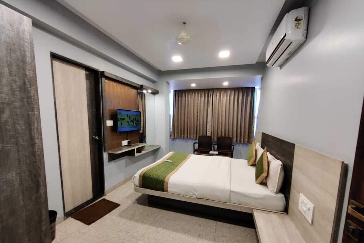A hotel room with a bed, a television, a desk, and a window with curtains.