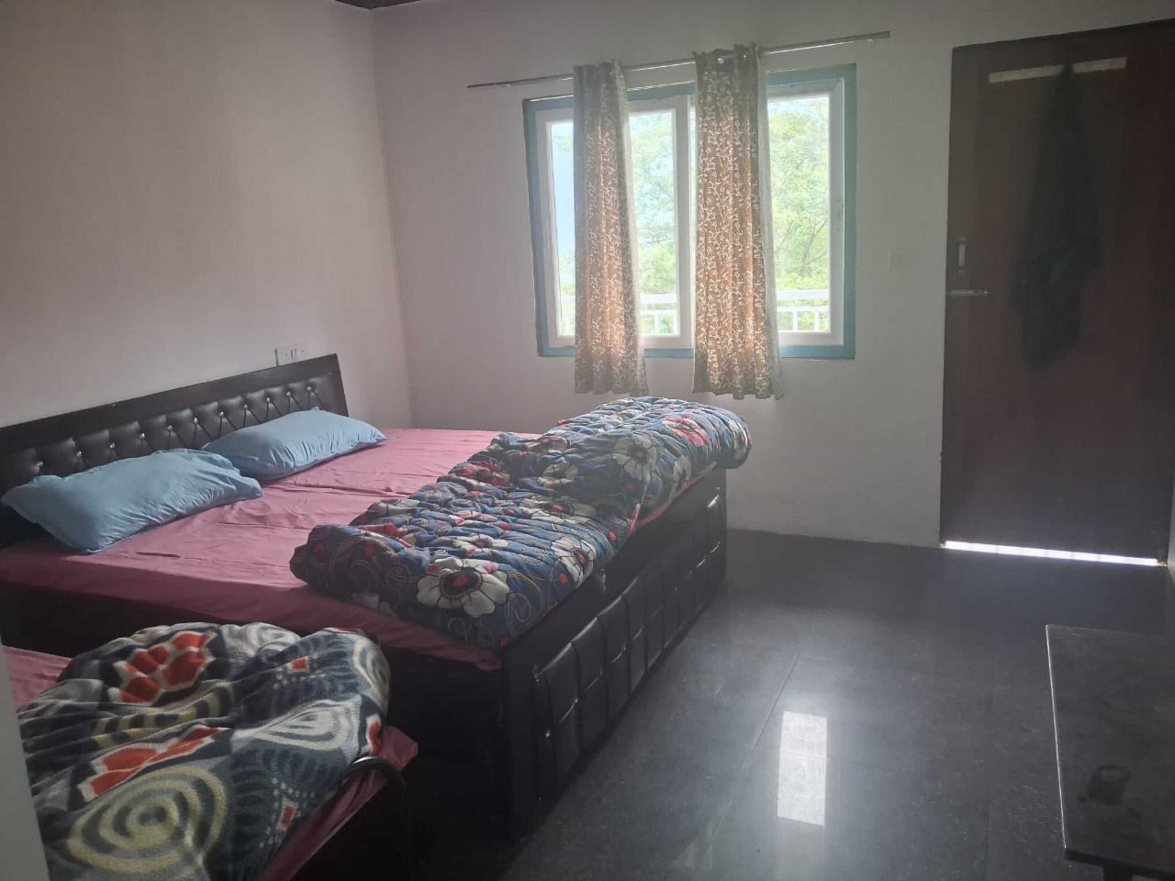 Una stanza con un letto, una panca, una finestra con tende e una porta.