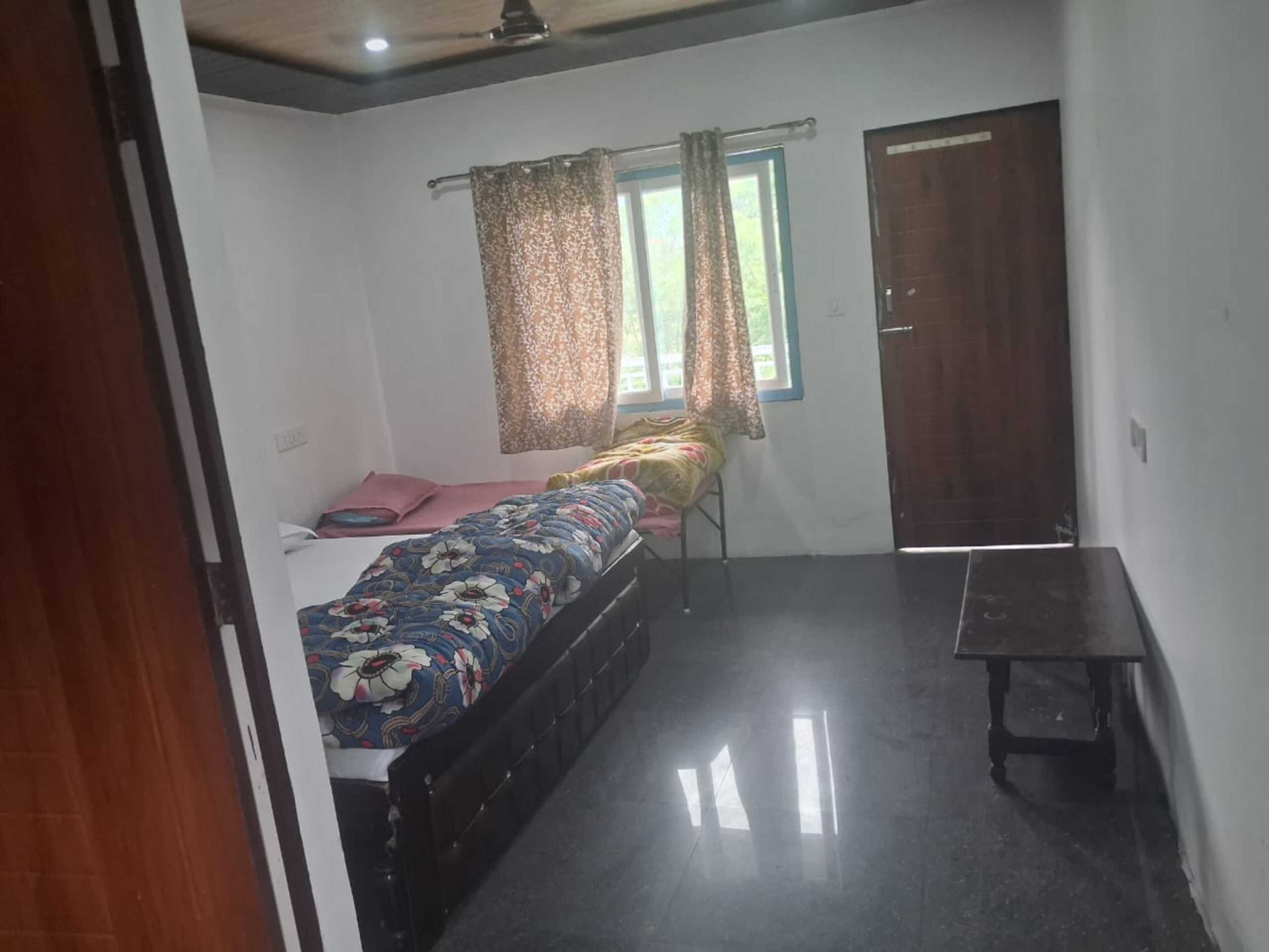 A bedroom with a bed, a window with curtains, a door, and a small table.