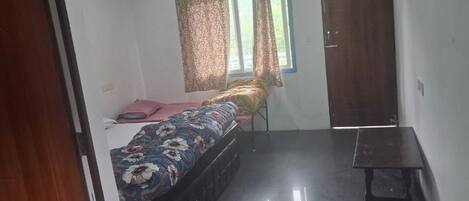 A bedroom with a bed, a window with curtains, a door, and a small table.