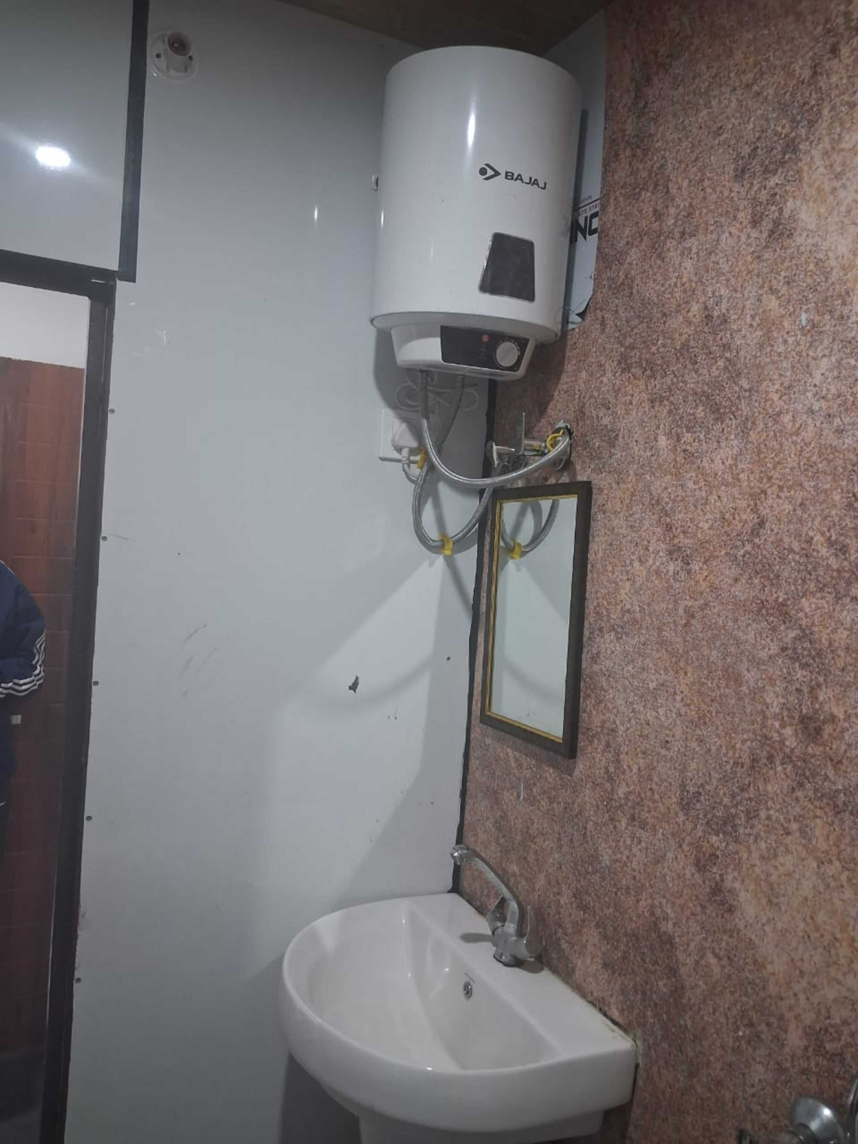 A bathroom with a white sink, a mirror, and a wall-mounted heater branded 'BAJAJ'.