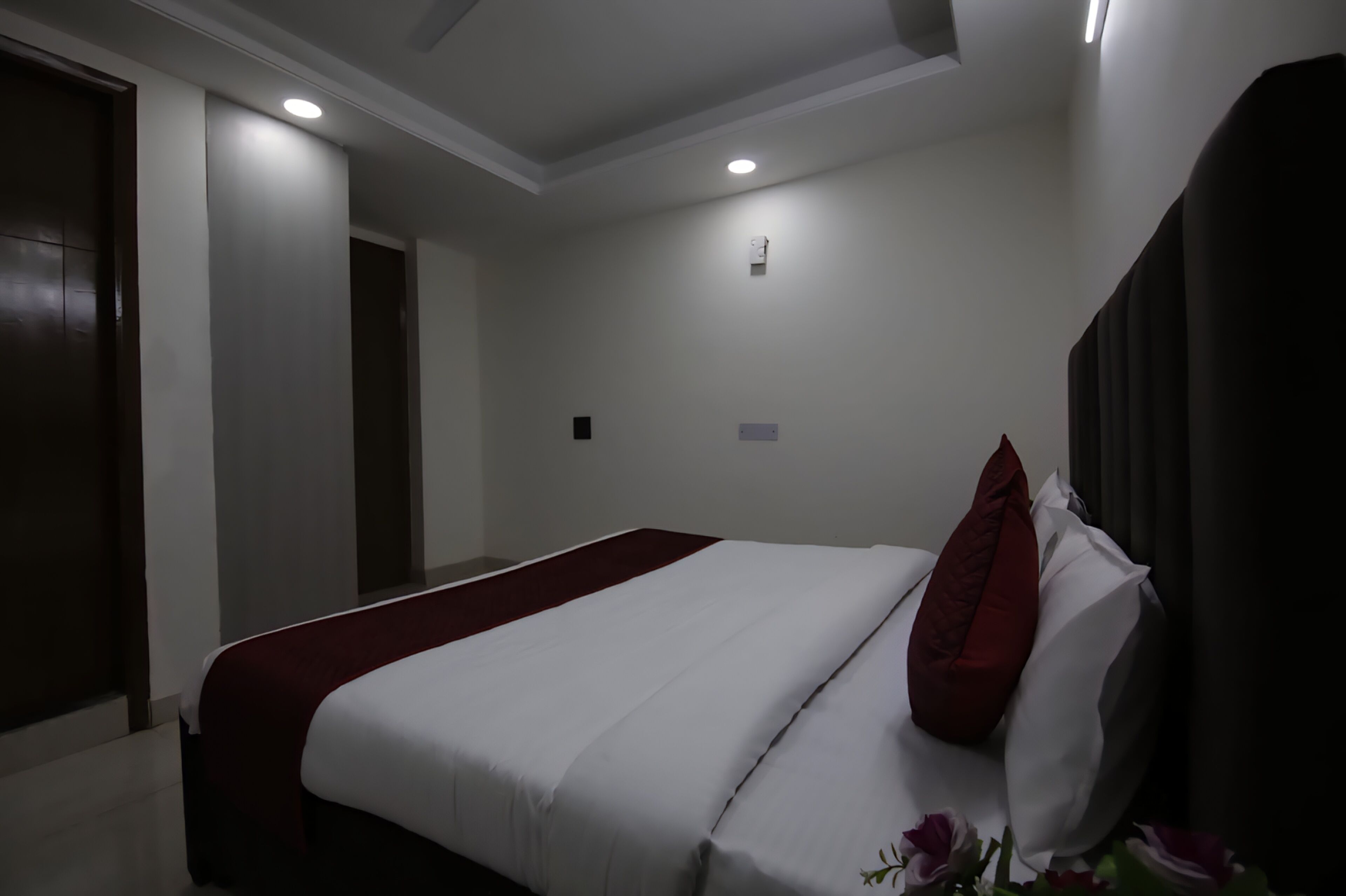 A hotel room with a bed, a red throw, a white pillow, and a small wall-mounted light.