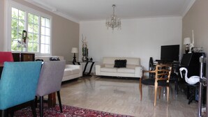 A living room with a white sofa, a dining table, a TV, and a chandelier.