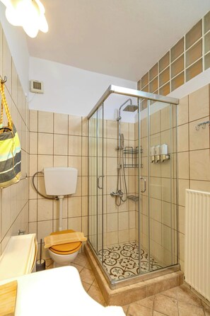A bathroom with a glass-enclosed shower, a toilet with a wooden seat, and a white bathtub. - Alkmene apartment - Warm Getaway in Kefalonia (Agia Effimia)