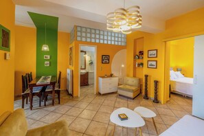 A compact living space with a dining area, a small seating area, a bed, and a staircase leading to an upper level. - Alkmene apartment - Warm Getaway in Kefalonia (Agia Effimia)