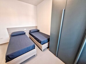 Ein kleines, modernes Zimmer mit zwei Einzelbetten, einem Kleiderschrank und Fliesenboden.
